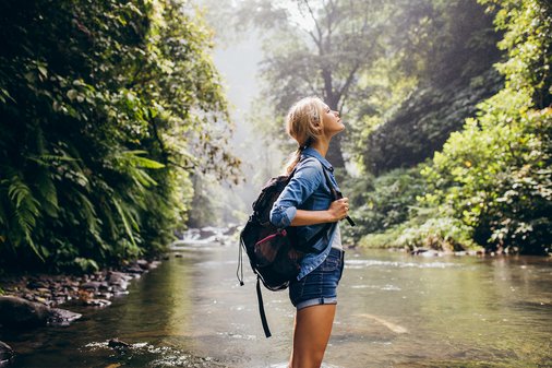 Frau schaut in die Luft an einer idyllischen Wasserquelle mitten in einem Wald 