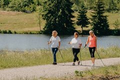 3 Nordic-Walking Läuferinnen gehen zusammen an einem Teich entlang