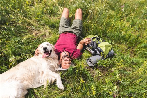 Mann liegt mit Hund auf einer Wiese