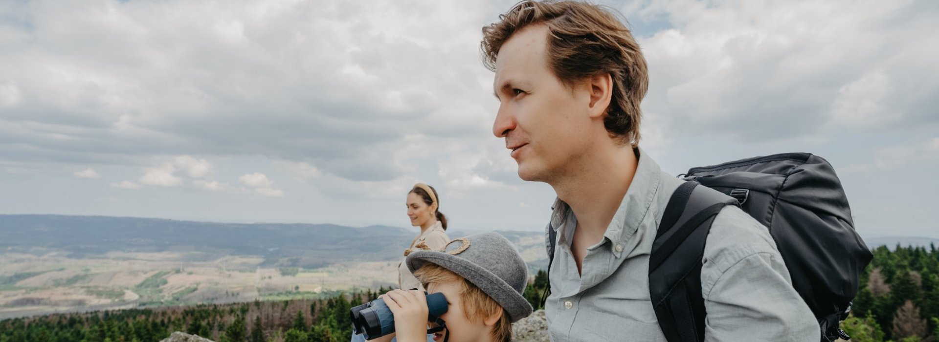 Familie steht auf einem steinigen Berg und schaut mit Fernglas über den Oberharz