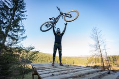 Mountainbiker steht auf einem Absprung und wirft sein Mountainbike in die Luft