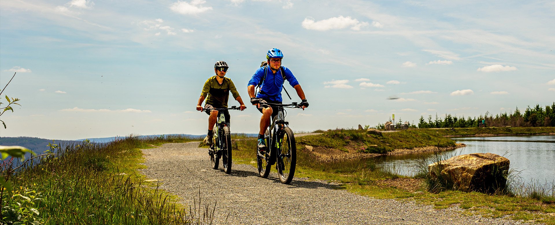 Zwei Radfahrer fahren auf einem steinigen Weg neben einem See entlang