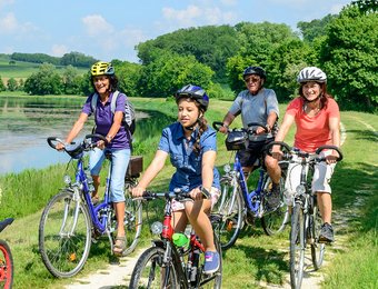Familie fährt zusammen mit dem Rad am Wasser aus dem Wald entlang