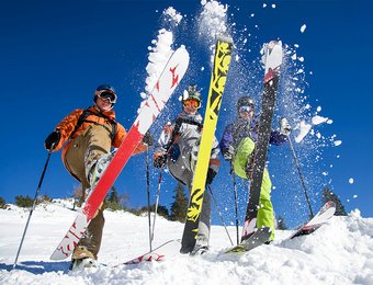 Drei Langläufer stecken ihre Ski in den Schnee und wirbeln diesen nach oben