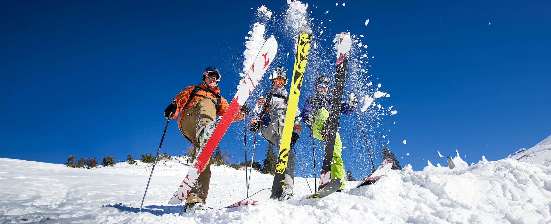 Drei Langläufer stecken ihre Ski in den Schnee und wirbeln diesen nach oben