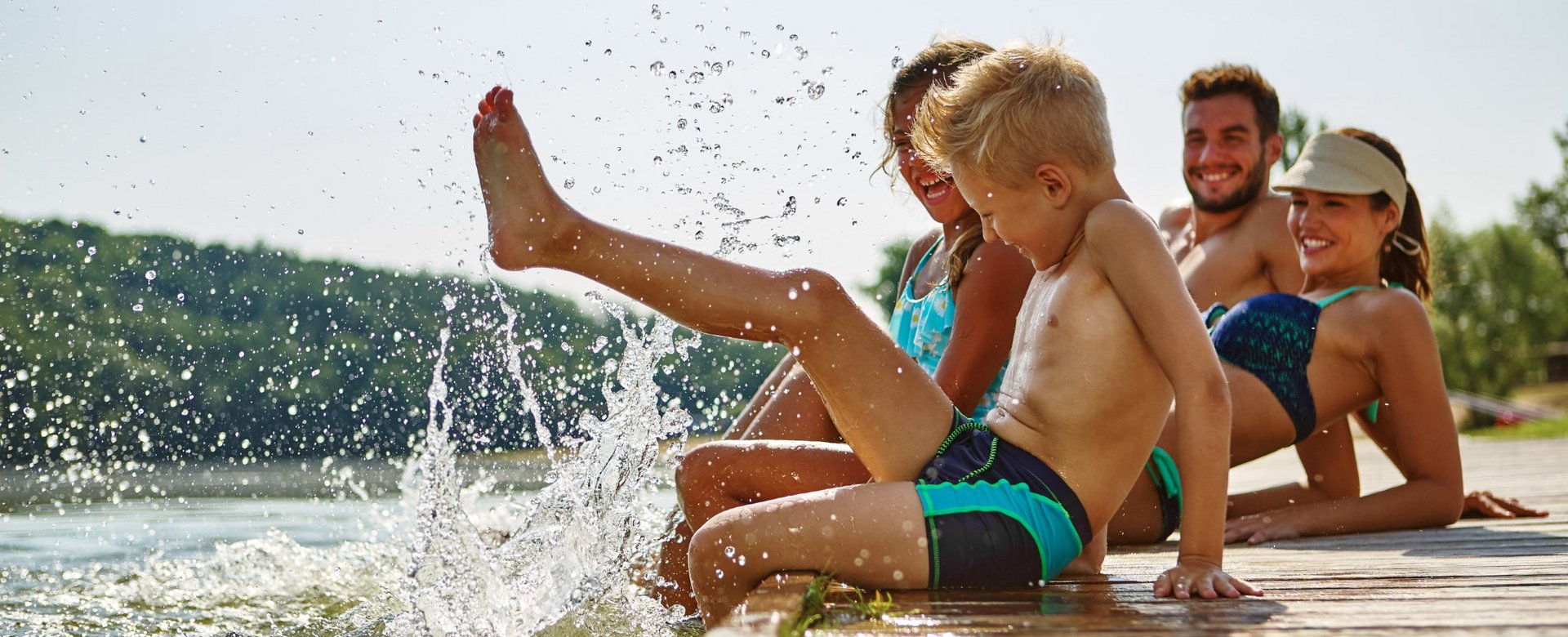 Kinder sitzen auf Steg und planschen mit den Füßen im Wasser 
