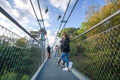 Personen stehen auf Hängebrücke und schauen auf vorbeirasende Personen an Zipline 