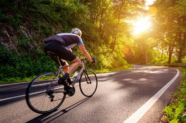 Rennradfahrer fährt bei Sonnenschein auf Straße entlang