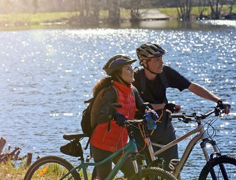 Frau und Mann stehen mit Mountainbike am Wasser und schauen in die Ferne