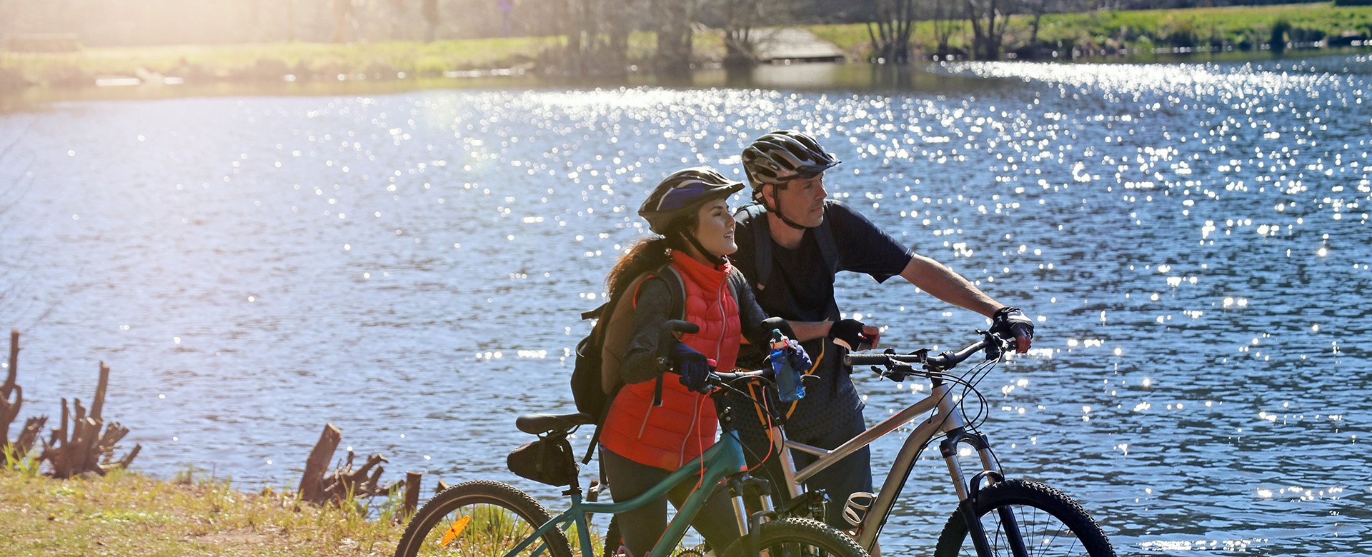 Frau und Mann stehen mit Mountainbike am Wasser und schauen in die Ferne