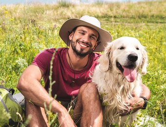 Mann mit Hund sitzen gemütlich auf einer hohen Wiese und lächeln in die Kamera