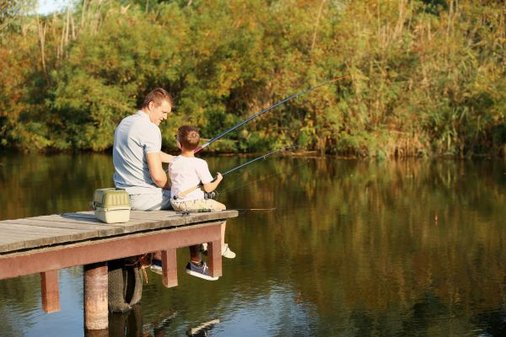 Vater und Sohn sitzen gemeinsam auf einem Steg und angeln 