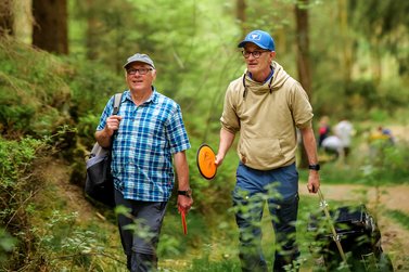 Zwei Männer laufen mit DiscGolf Scheibe in der Hand durch einen Wald