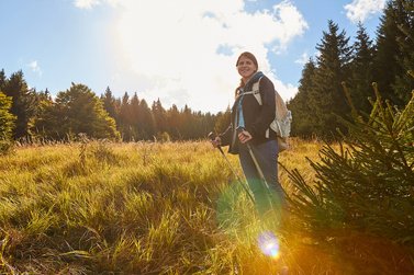 Frau steht mit Nordic-Walking Stöcken im Wald bei sonnigem Wetter