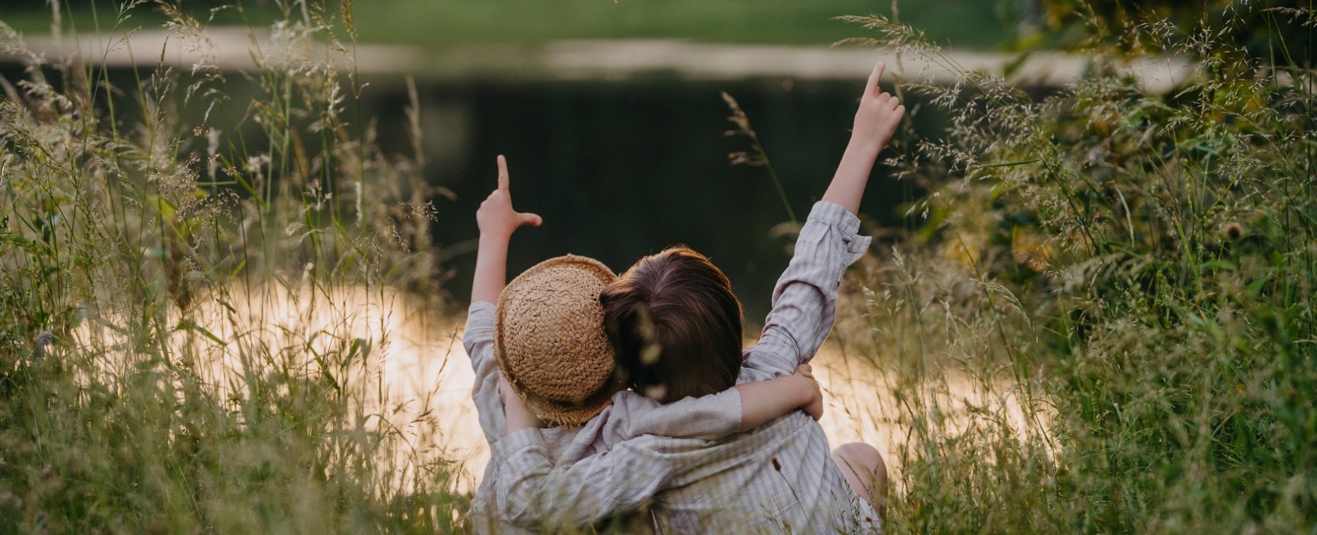 Kinder sitzen im hohen Gras am Uferrand und zeigen in die Luft