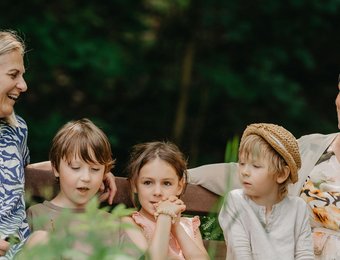 Kinder mit Frauen sitzen auf einer Bank und freuen sich