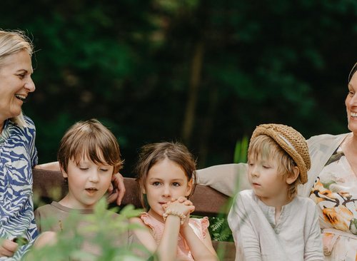 Kinder mit Frauen sitzen auf einer Bank und freuen sich