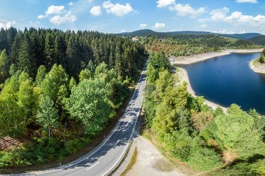 Luftaufnahme einer Straße direkt neben einem Wald und einem See