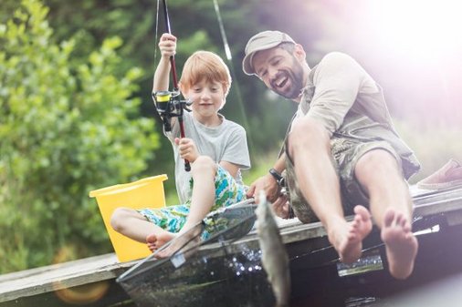 Mann und Junge sitzen auf einem Steg und haben einen Fisch an der Angelrute