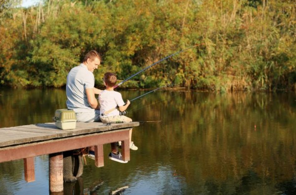 Vater und Sohn sitzen gemeinsam auf einem Steg und angeln 