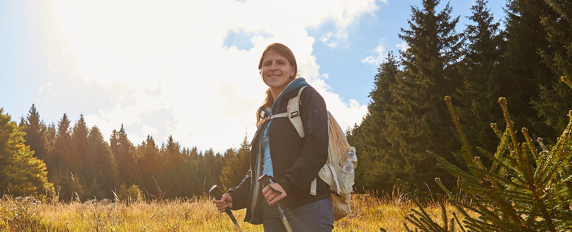 Frau mit Nordic-Walking Stöcken steht bei einem sonnigen Tag im Wald