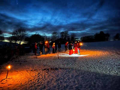 Menschen stehen im Schnee bei Fackelschein und warten auf die Fackelwanderung als Alternativprogramm zum Schlittenhunderennen
