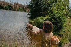 Kind steht vor einem See und zeigt mit einem Arm auf das Wasser