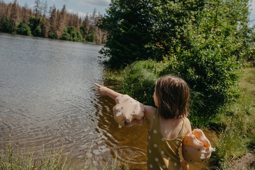 Kind steht vor einem See und zeigt mit einem Arm auf das Wasser