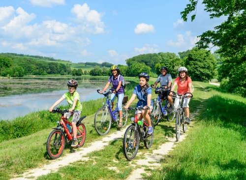 Familie mit Kindern fährt zusammen an einem See mit dem Rad entlang