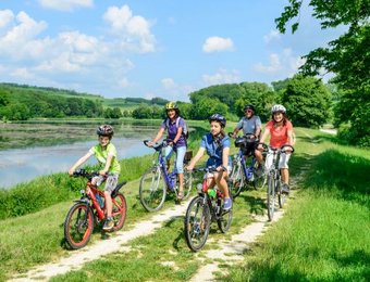 Familie mit Kindern fährt zusammen an einem See mit dem Rad entlang