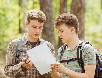 2 junge Männer stehen im Wald und schauen auf Wanderkarte 