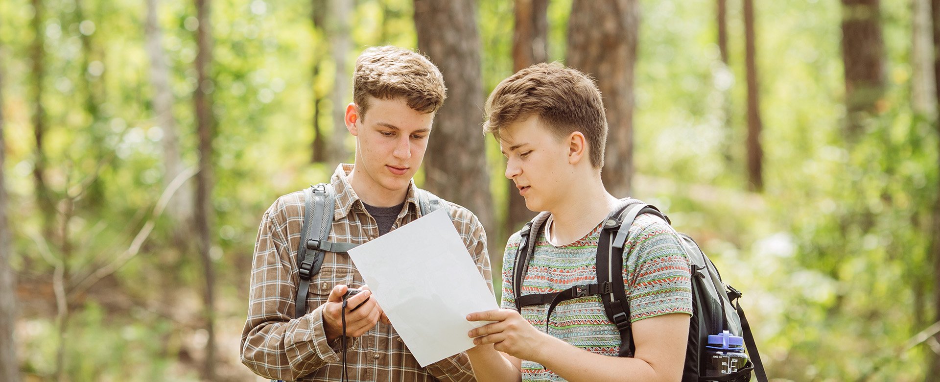 2 junge Männer stehen im Wald und schauen auf Wanderkarte 