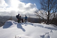 Familie steht mit einem Hund auf einer Schneebedeckten Bergkuppe mit Weitblick