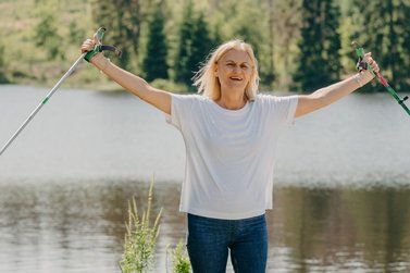 Nordic-Walking Läuferin freut sich und hebt beide Arme mit Stöcken in den Händen