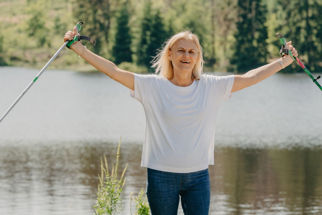 Nordic-Walking Läuferin freut sich und hebt beide Arme mit Stöcken in den Händen