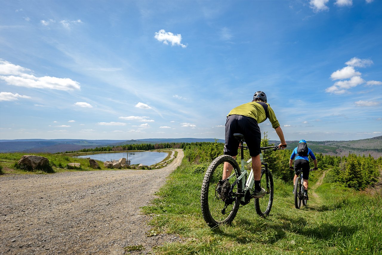 Zwei Mountainbiker fahren vom Schotterweg ab auf einen Offroad Weg