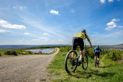 Zwei Mountainbiker fahren vom Schotterweg ab auf einen Offroad Weg