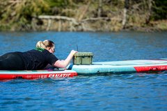 Teilnehmerin liegt auf SUP und öffnet eine Kiste 