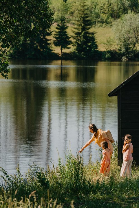 Mutter mit zwei Kindern steht am Ufer eines Sees inmitten Sommerlicher Natur