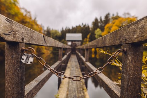 Schloss mit Kette welche den Zugang zu einem Steg versperrt welcher über Wasser zu einem kleinen Häuschen führt