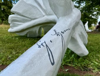 große Feder-Skulptur auf einer Wiese mit Fokus auf eine Unterschrift darauf