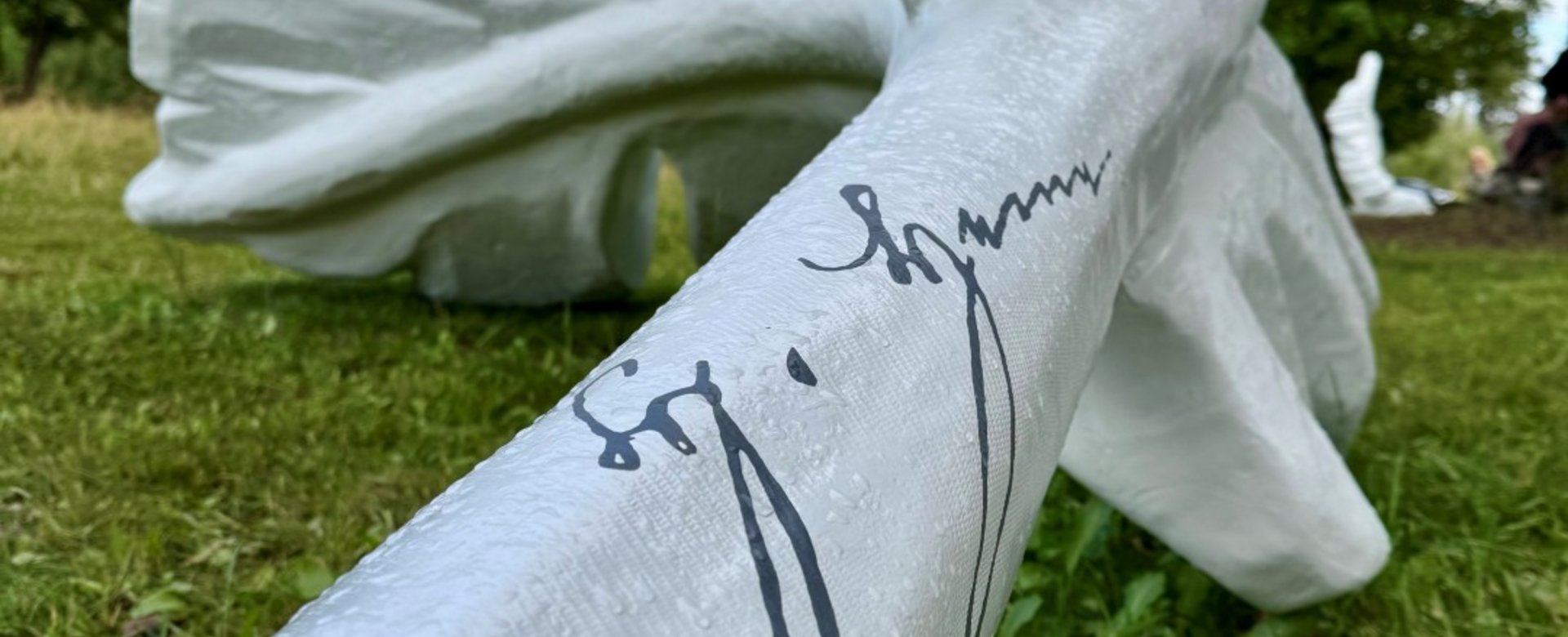 große Feder-Skulptur auf einer Wiese mit Fokus auf eine Unterschrift darauf