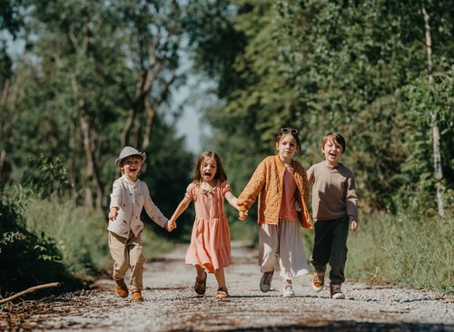 Kinder halten sich an den Händen und rennen einen Wanderweg entlang