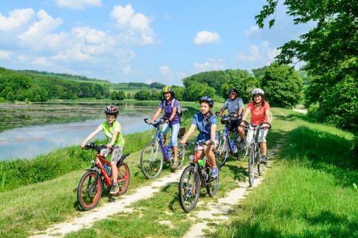 Familie mit Kindern fährt zusammen an einem See mit dem Rad entlang